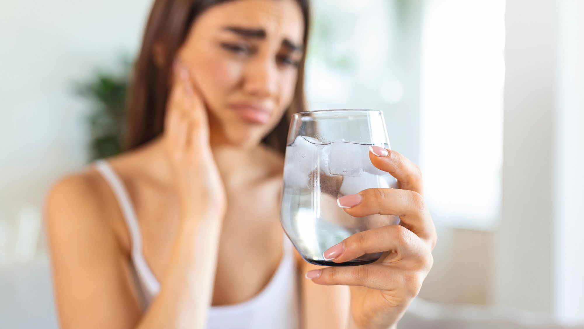 A girl holding a glass of ice water and unable to drink due to sudden tooth sensitivity