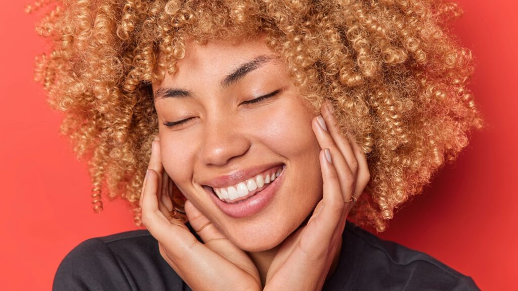 A woman with curly hair smiling and showing off her bright smile after a successful teeth whitening treatment