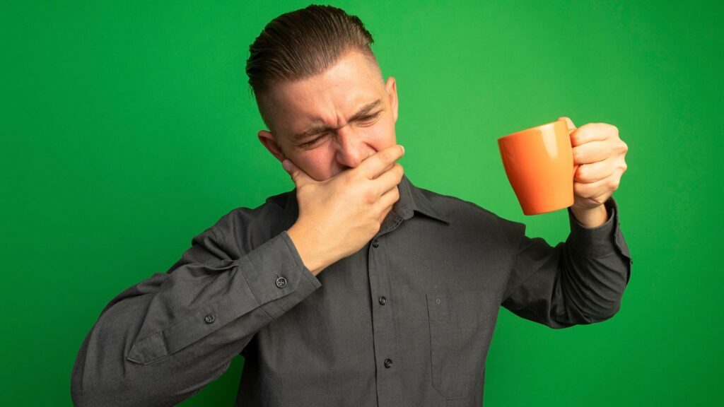 A boy holding a hot cup of tea, displeased to drink it because of teeth sensitivity