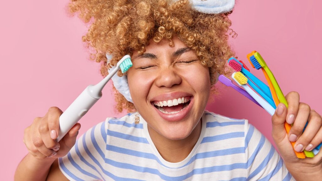 A woman smiling and holding an electric and manual toothbrushes to maintain good oral hygiene