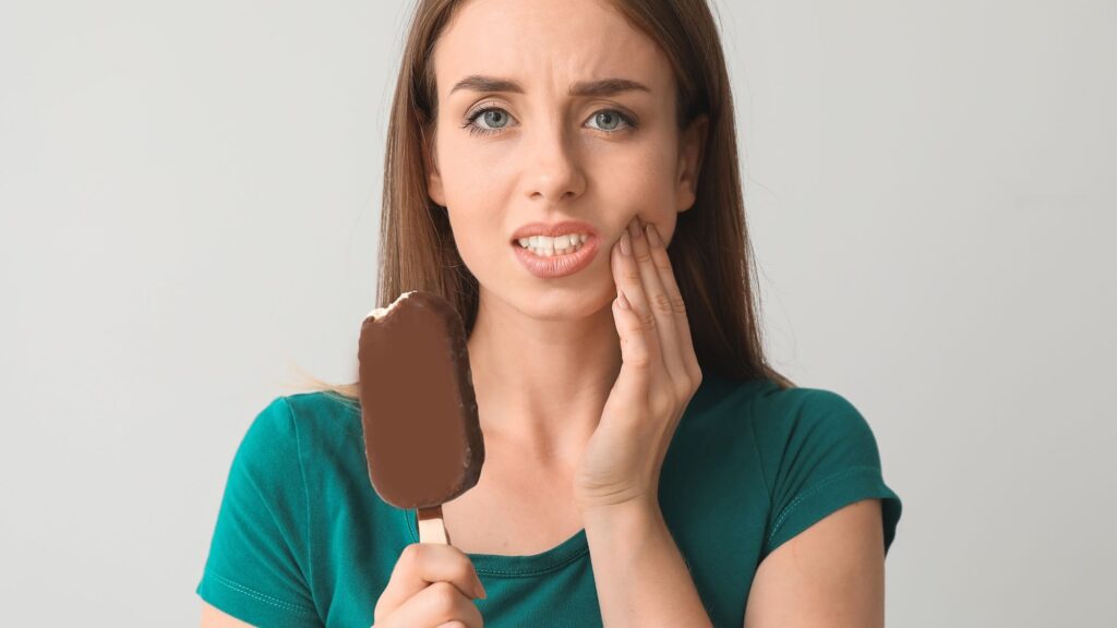A girl holding her mouth while holding an ice cream because of sensitive teeth pain