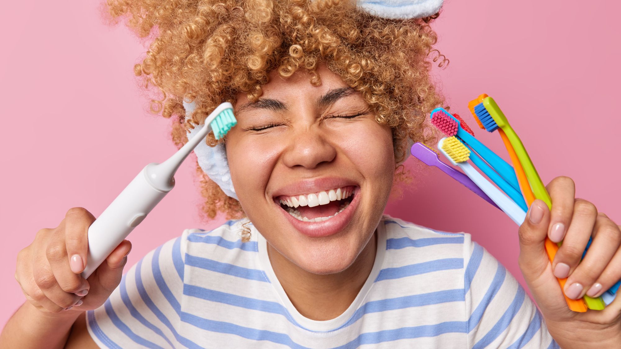 A girl in joy, holding an electric toothbrush and a couple of manual toothbrushes
